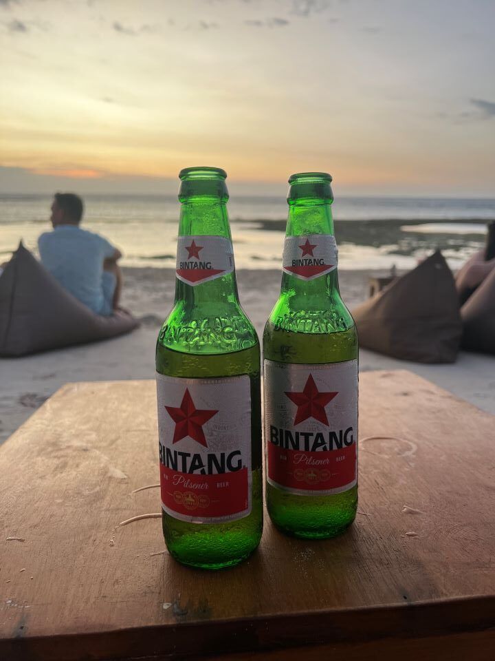 ruta por indonesia dos cervezas en un mesa en un atardecer cerca del mar de fondo